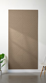 Light brown Felt Right 4’ x 8’ PET felt panel with geometric lines engraved into the material against a white wall. A plant and chair are in the foreground.