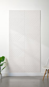 White Felt Right 4’ x 8’ PET felt panel with geometric lines engraved into the material against a white wall. A plant and chair are in the foreground.