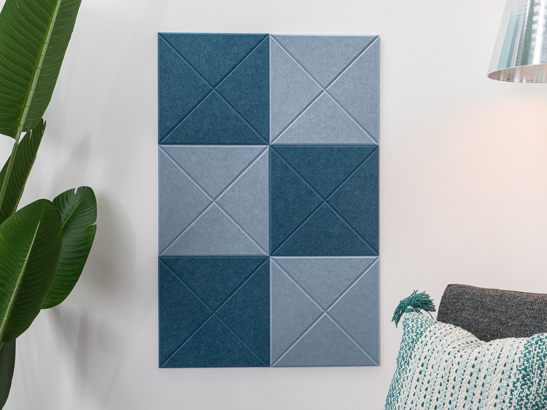 Felt Right wall art design using shades of blue squares with beveled x's on a white wall next to a house plant and a chair.