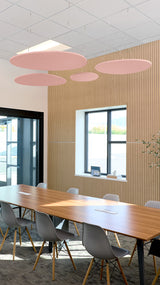 Four pink cloud-shaped ceiling baffles suspended above a conference table in an office space.