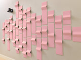 Multiple pink 3D tiles arranged in a dimensional peak pattern on a beige wall with a small black object in the corner.