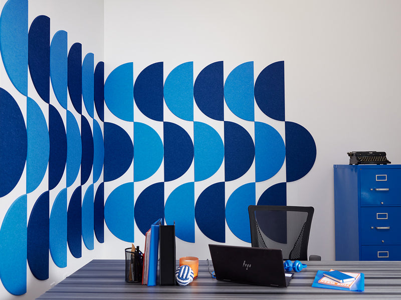 Felt Right wall tiles using half circle shapes in shades of blue creating a geometric pattern on a white walls by a desk and a filing cabinet in the corner.