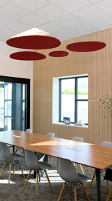 Four burgundy oval acoustic baffles suspended from ceiling in modern office conference room.