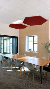 Two dark red hexagonal acoustic panels suspended from ceiling above conference table in office space.