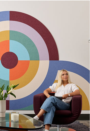 Woman sitting in a modern chair in front of a colorful abstract wall mural.