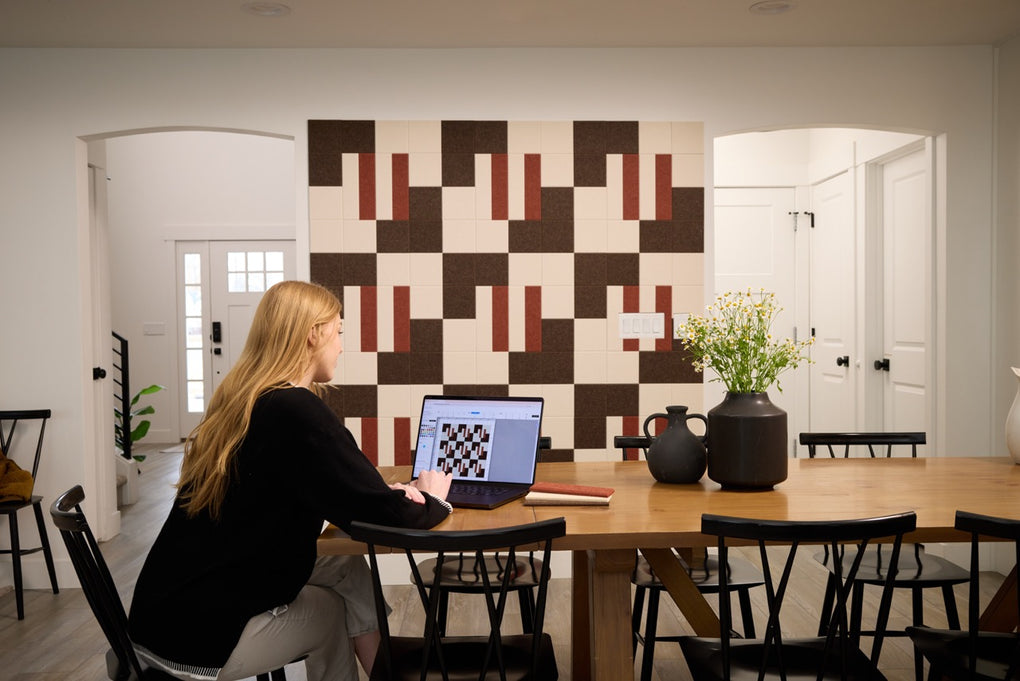 Woman using the Felt Right Design Studio on a laptop at her kitchen table to customize the Alto design. It has warm colors like cream, brown, and burnt orange.
