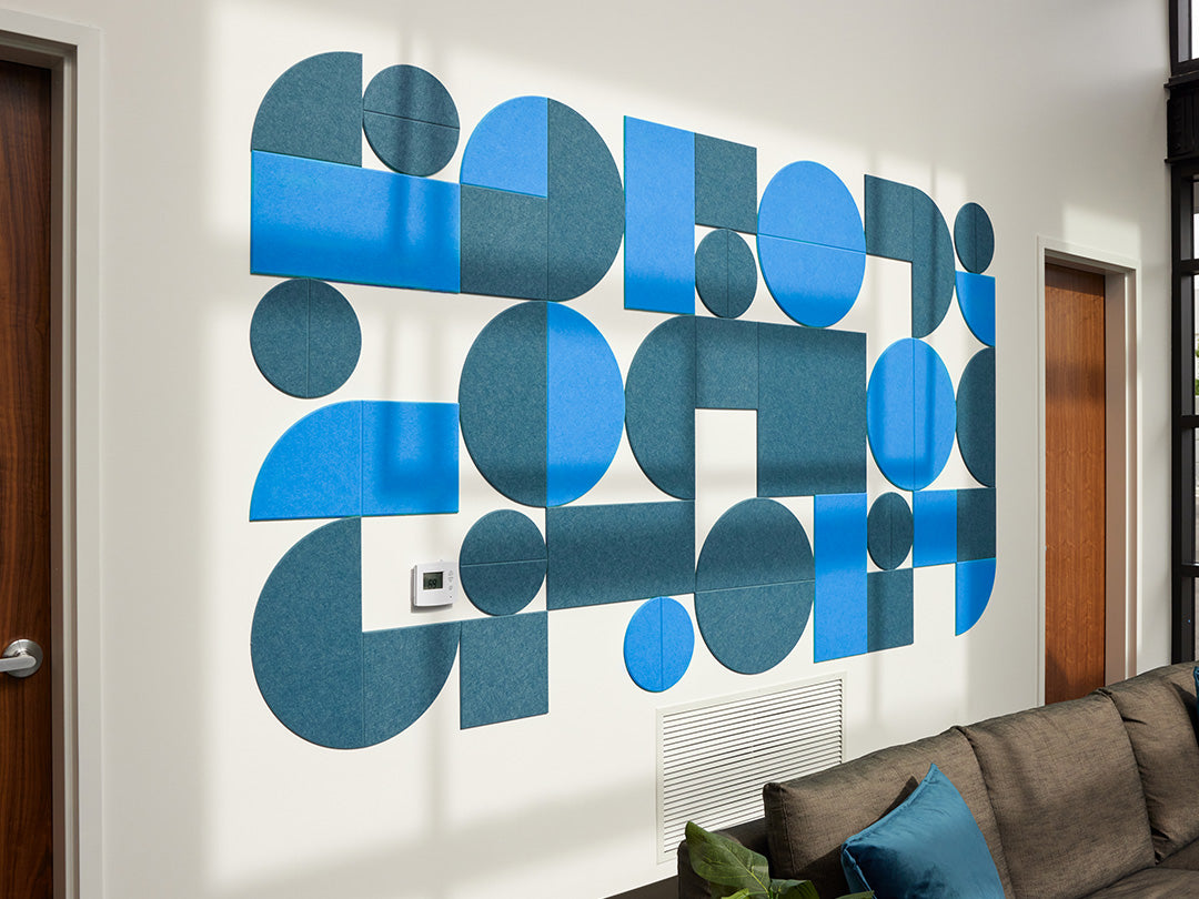 A Felt Right wall art design in shades of blue using circles and squares to create geometric design on an office wall with a couch.
