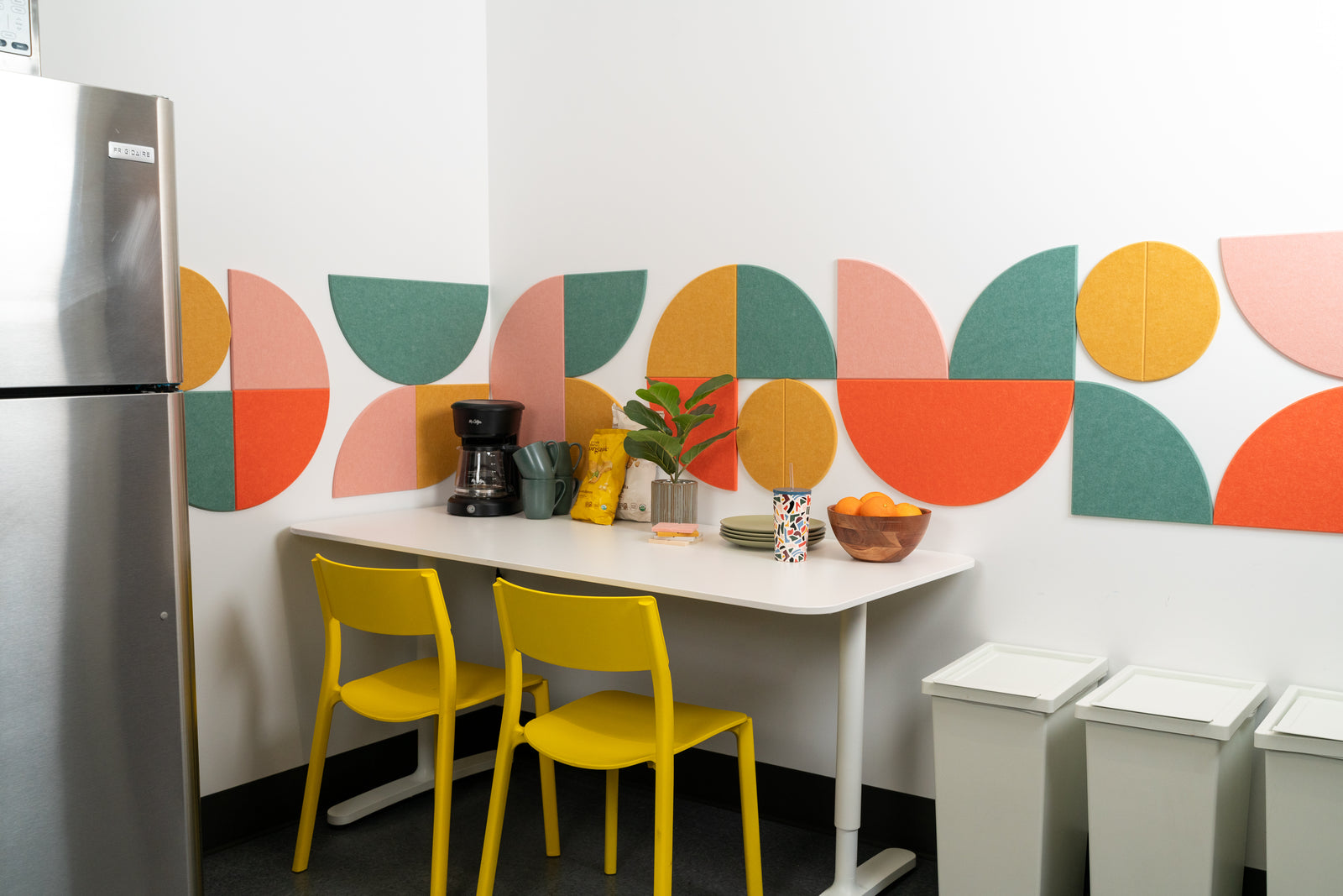 A Felt Right wall art design using circles in shades of green, orange, and yellow to create a geometric pattern in a kitchen above a table.