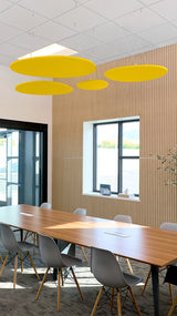 Four yellow oval acoustic baffles suspended from ceiling above conference table in office space.