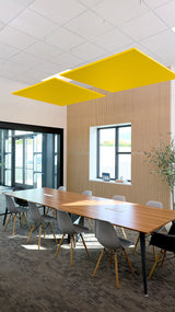 Two yellow flat square acoustic baffles suspended from ceiling above conference table in modern office space.