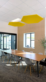 Two yellow hexagon-shaped acoustic baffles suspended from ceiling above conference table in modern office space.