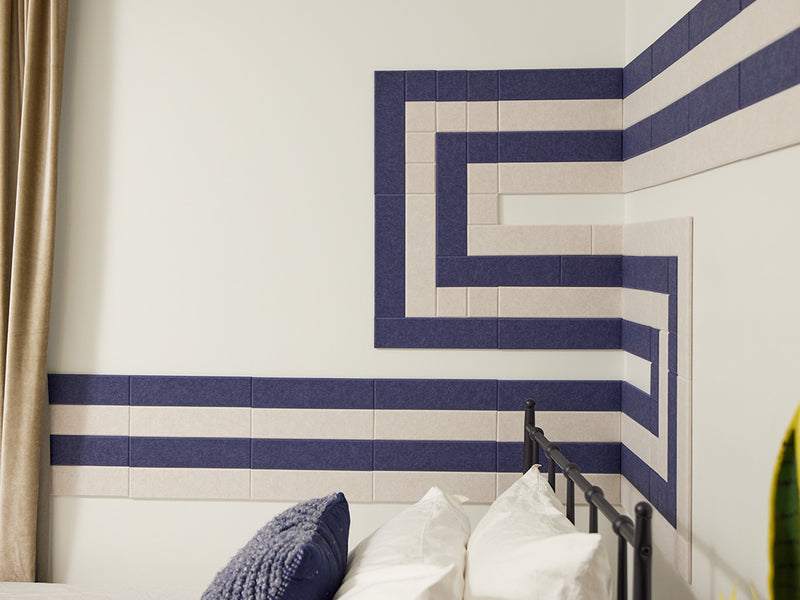 Felt Right wall art tiles in shade of blue and cream in a pipeline pattern  in a bedroom with a bed and curtains