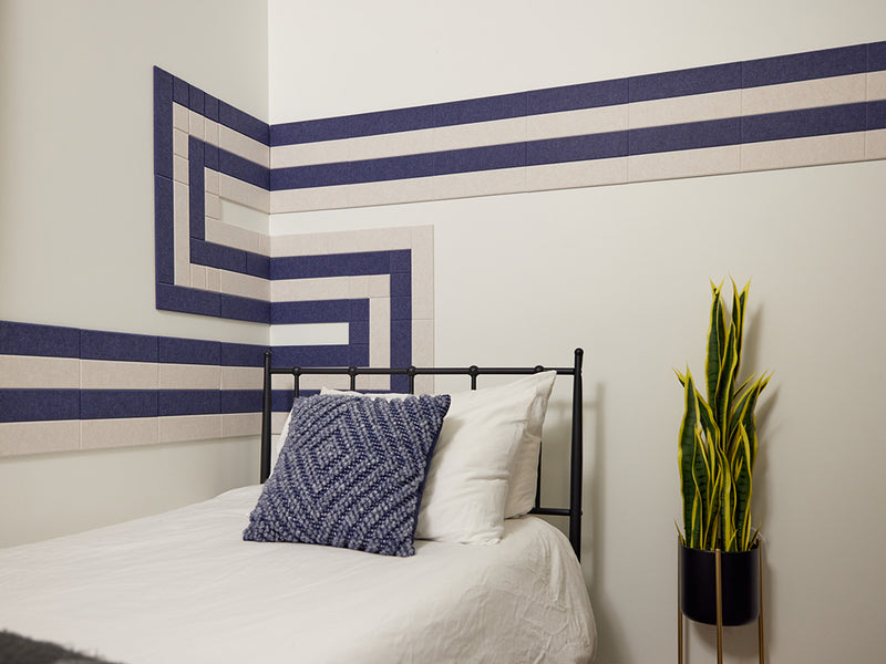 Felt Right wall art tiles in shade of blue and cream in a pipeline pattern  in a bedroom with a bed and a house plant