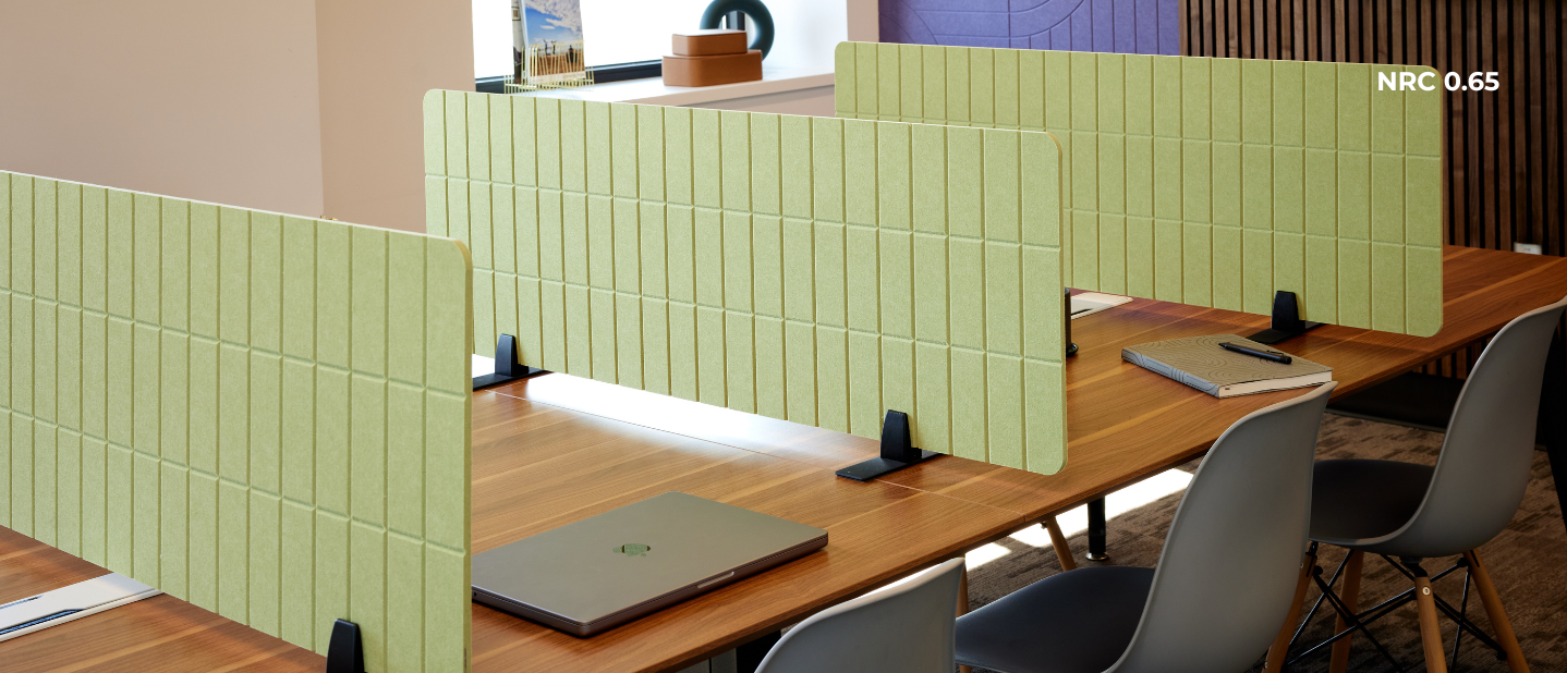 Green office partitions separating desks with laptops and chairs.