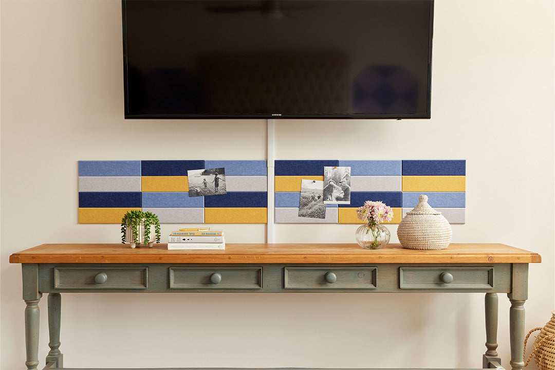 A Felt Right wall art design in shades of blue and yellow creating a pinnable wall art above a side stable and below a tv mounted on the wall.