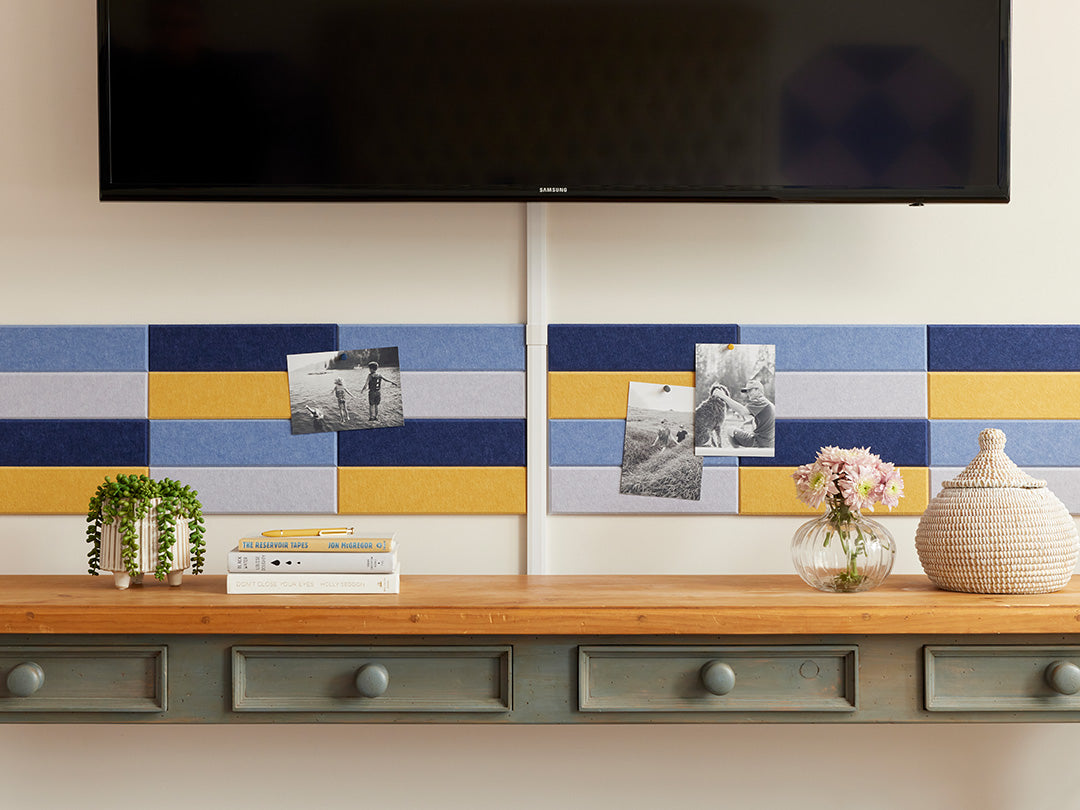 A Felt Right wall art design in shades of blue and yellow creating a pinnable wall art above a side stable and below a tv mounted on the wall.