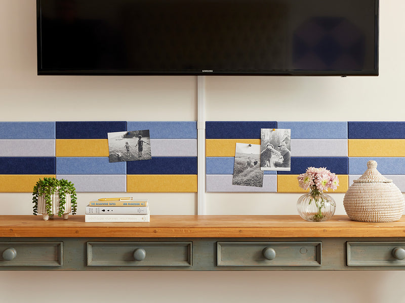 A Felt Right wall art design in shades of blue and yellow creating a pinnable wall art above a side stable and below a tv mounted on the wall.