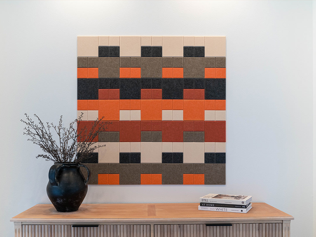 Colorful geometric wall art above a wooden cabinet with a vase and books.