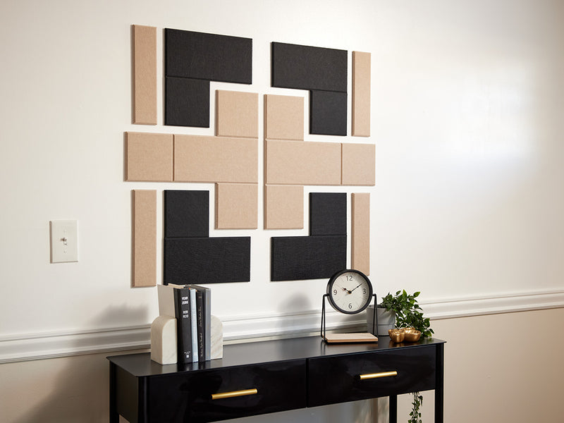 A Felt Right design on a wall above a table with books and a clock on it in shades of tan and black felt tiles