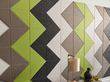 A Felt Right wall art design using shades of brown green and gray felt  on a white wall and a  side table with a lamp in front.