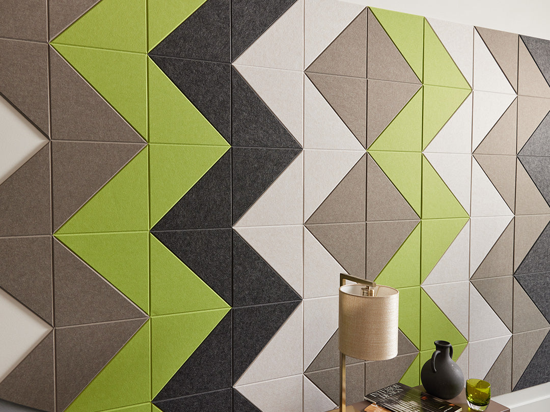A Felt Right wall art design using shades of brown green and gray felt  on a white wall and a  side table with a lamp in front.