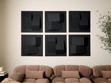 Six black square tiles with three-dimensional geometric shapes arranged in a grid on a wall above a tan sofa.