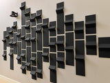 Black 3D dimensional tiles arranged in an abstract pattern on a white wall with varying depths and angles.
