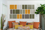 Modular wall art display with orange, green, cream, and brown fabric panels arranged in grid pattern above seating area with 