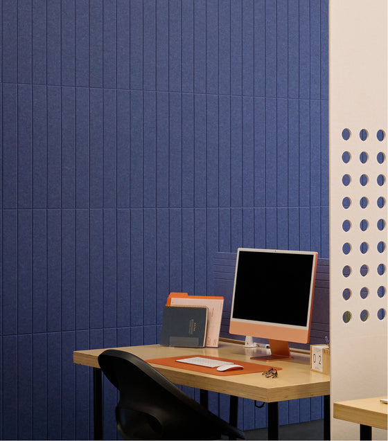 Modern office setup with a desk, computer monitor, and chair against a blue tiled wall.