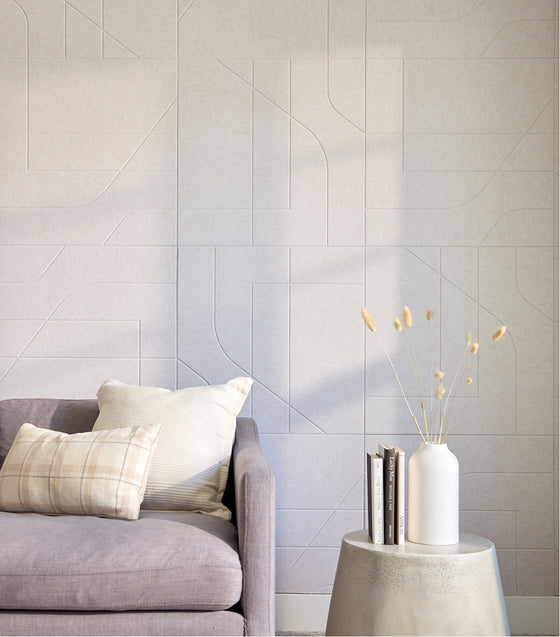 Gray sofa with a white pillow against a light gray wall with geometric patterns.