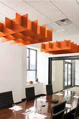 Orange 3D grid baffles suspended from ceiling in modern office meeting room above conference table.
