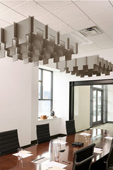 Two gray 3D cloud-shaped acoustic baffles suspended from drop ceiling in office conference room above wooden table.