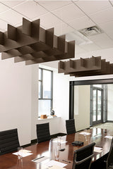 Brown geometric acoustic baffles suspended from ceiling grid above conference table in office space.