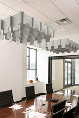 Gray modular acoustic baffles suspended from ceiling in staggered 3D arrangement above conference table.