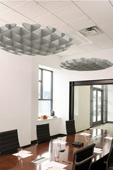 Silver 3D cloud-shaped acoustic baffles suspended from ceiling in conference room above wooden table.