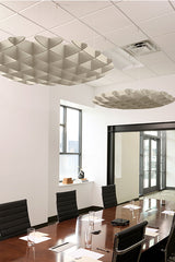 Two metallic 3D cloud-shaped acoustic baffles suspended from a drop ceiling in an office conference room.
