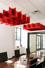 Red geometric 3D cloud baffles suspended from white ceiling grid in modern office conference room.