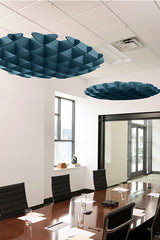 Two teal 3D cloud-shaped acoustic baffles suspended from a drop ceiling in a conference room with a wooden table and black ch