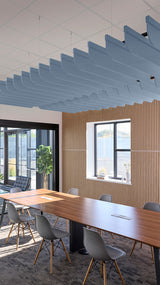 Blue fin-shaped acoustic baffles suspended from ceiling in modern office meeting room with wooden table and chairs.