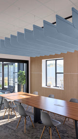 Blue curved acoustic baffle panels suspended from ceiling above conference table in office space.