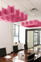 Pink 3D cloud-shaped acoustic baffles suspended from ceiling above conference table in office space.