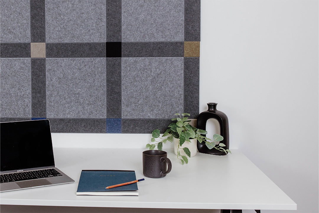 Pinnable Felt Right sound absorbing pinboard in a colorway that encourages focus. It has greys, blues, and neutrals. This pinboard is located behind a white desk with a computer on the desktop.