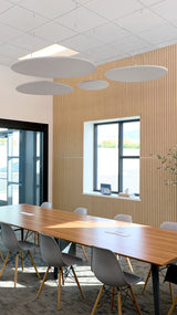 Gray oval ceiling baffles suspended in conference room with wood slat wall and dining table.