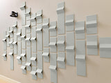 Light gray three-dimensional tiles arranged in an ascending pattern on a beige wall with a black object in upper left corner.