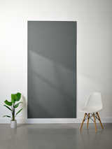 Dark gray felt sheet mounted on white wall with plant and white chair beside it.