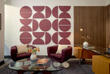 A Felt Right wall art design using large half circles in a dark red shade on a white wall  in an office with a desk and two accent chairs.