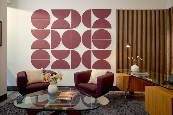 A Felt Right wall art design using large half circles in a dark red shade on a white wall  in an office with a desk and two accent chairs.