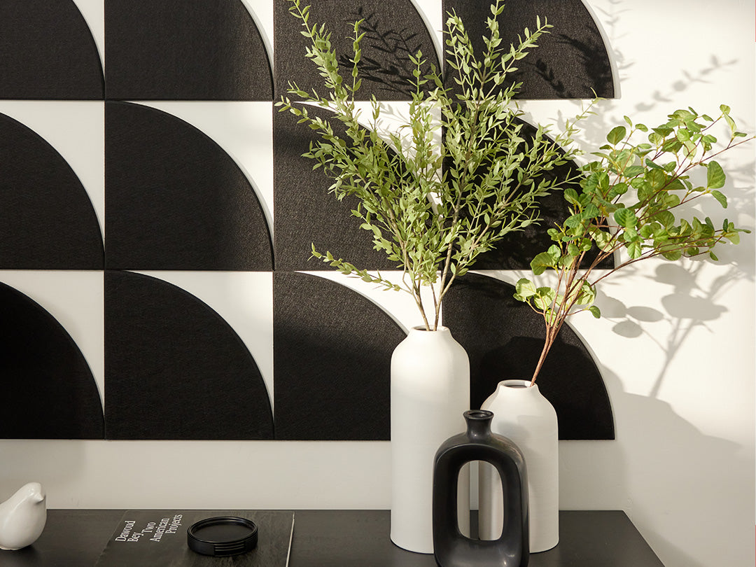Two white vases with green plants against a black and white geometric wall.