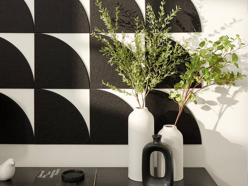 Two white vases with green plants against a black and white geometric wall.