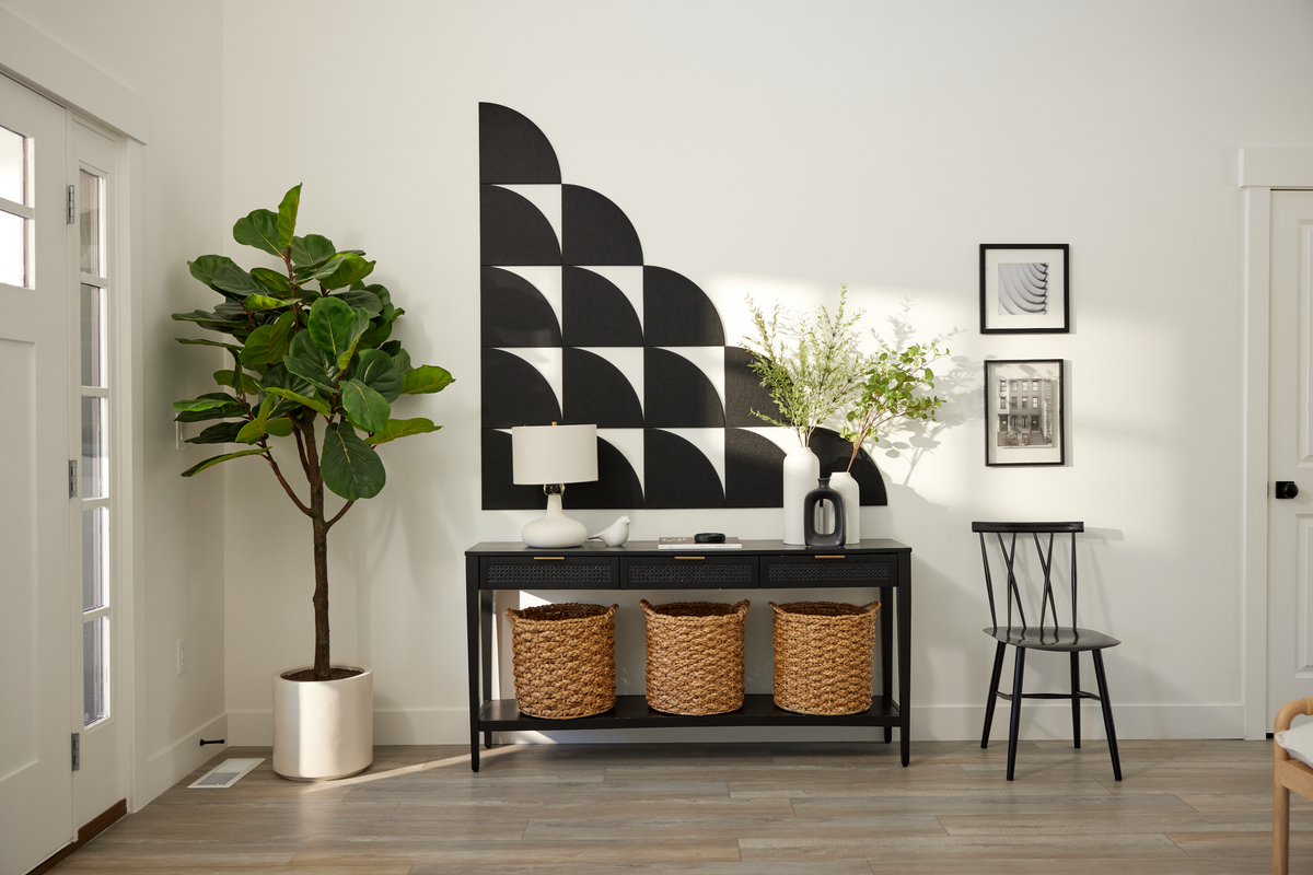 A Felt Right wall art design using black quarter circles to create a geometric slope pattern on a white wall at the entry of a home above a table with decor and a house plant in the corner.